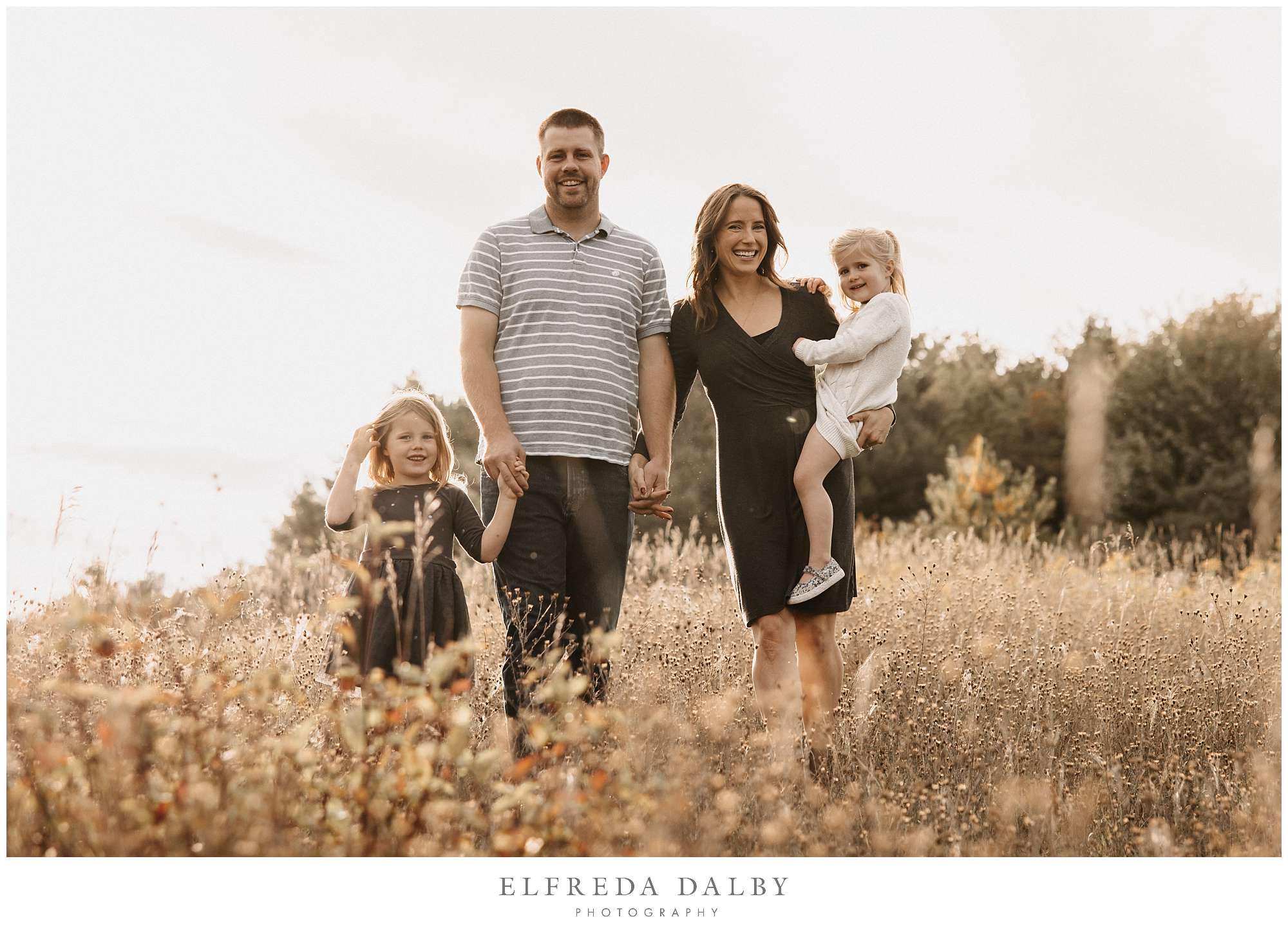 A family of four walking through a field during golden hour